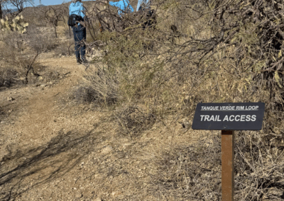 Image shows two hikers passing a sign that marks the beginning of the Tanque Verde Rim Loop.