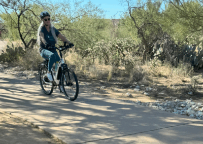 Image shows a woman on a bicycle along the sidewalk portion of the trail.