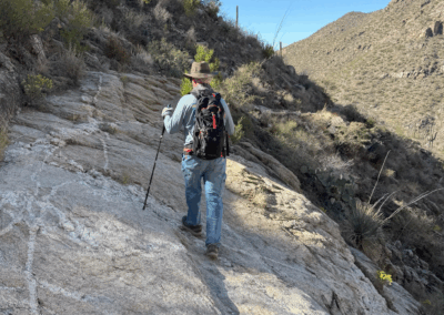 Image shows a hiker walking along a lengthy, steep rock outcrop on the trail.