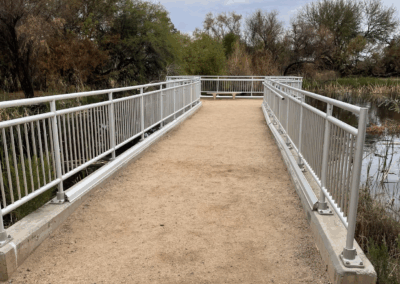 Image shows a railed viewpoint extending into the pond with a packed granite surface and safety railing.