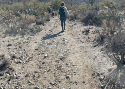Image shows a hiker walking along a semi-rocky flat trail.