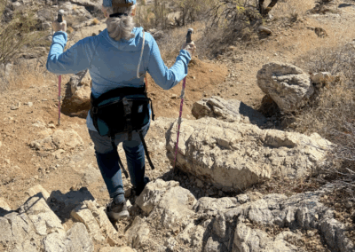 Image shows a female hiker with poles on a rocky section of the trail.