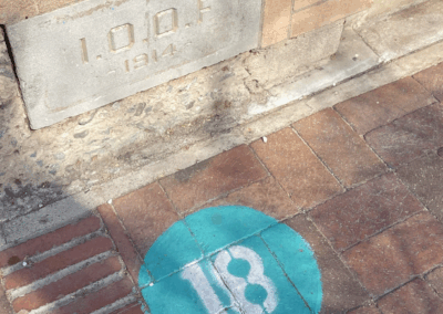 Image of the number 18 painted in a cyan circle on a sidewalk.