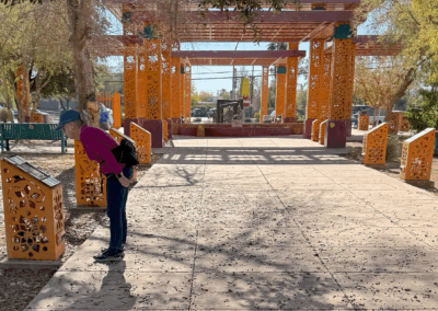 Image of an elderly woman reading an interpretive sign under the shade of a tree along a sidewalk.