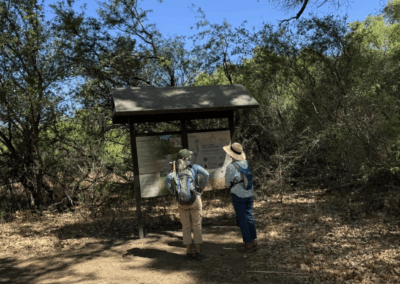 Image of hikers looking at a large interpretive sign along the dirt trail.