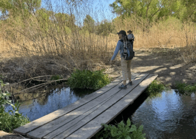 Image of a hiker on a narrow wooden bridge crossing the river.