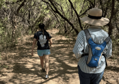 Image of two hikers going through a shady passage through a mesquite bosque.
